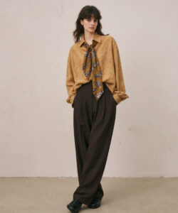 In A Tan Blouse Floral Scarf Brown High Waisted Pants Black Shoes Against A