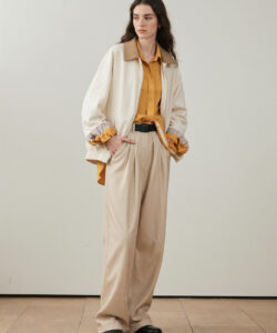 Long Haired Woman In A Yellow Shirt White Jacket Beige Pants Black Shoes Against