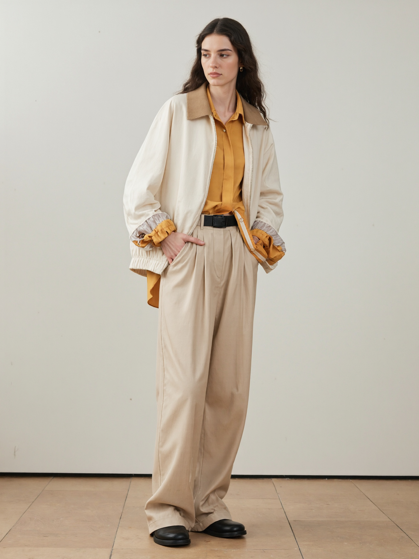 Long Haired Woman In A Yellow Shirt White Jacket Beige Pants Black Shoes Against