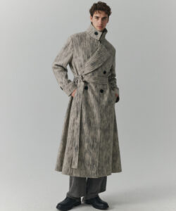 Man In A Textured Grey Overcoat Grey Pants And Black Shoes Standing Against A