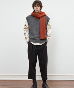 Man With Curly Hair Wearing A Gray Vest Orange Scarf Floral Shirt Black Pants