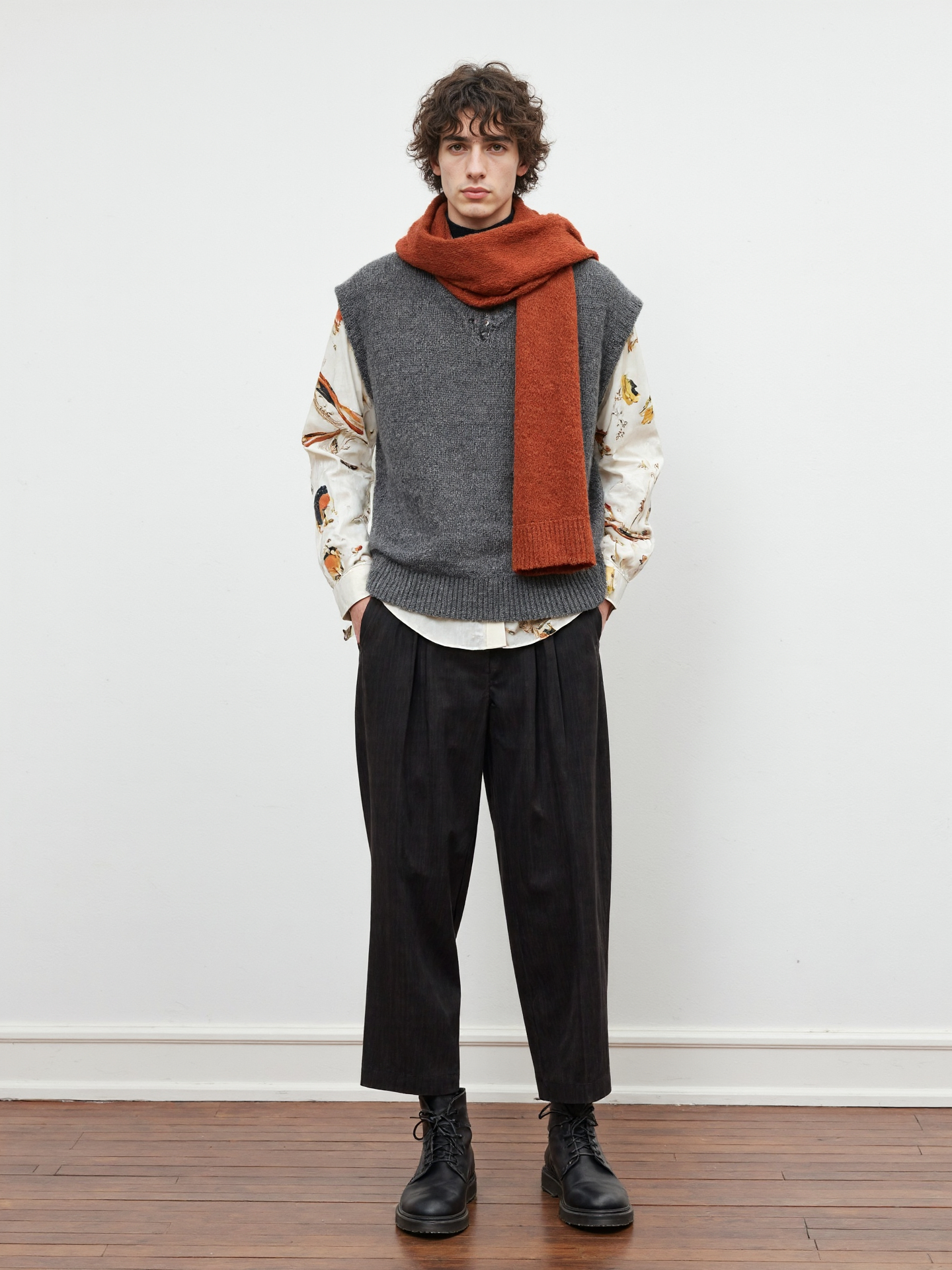 Man With Curly Hair Wearing A Gray Vest Orange Scarf Floral Shirt Black Pants