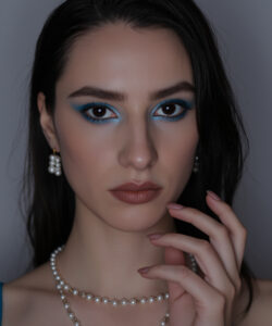 Pale Skinned Woman With Dark Hair Blue Blue Eyeshadow And Pearl Necklaces Set Against