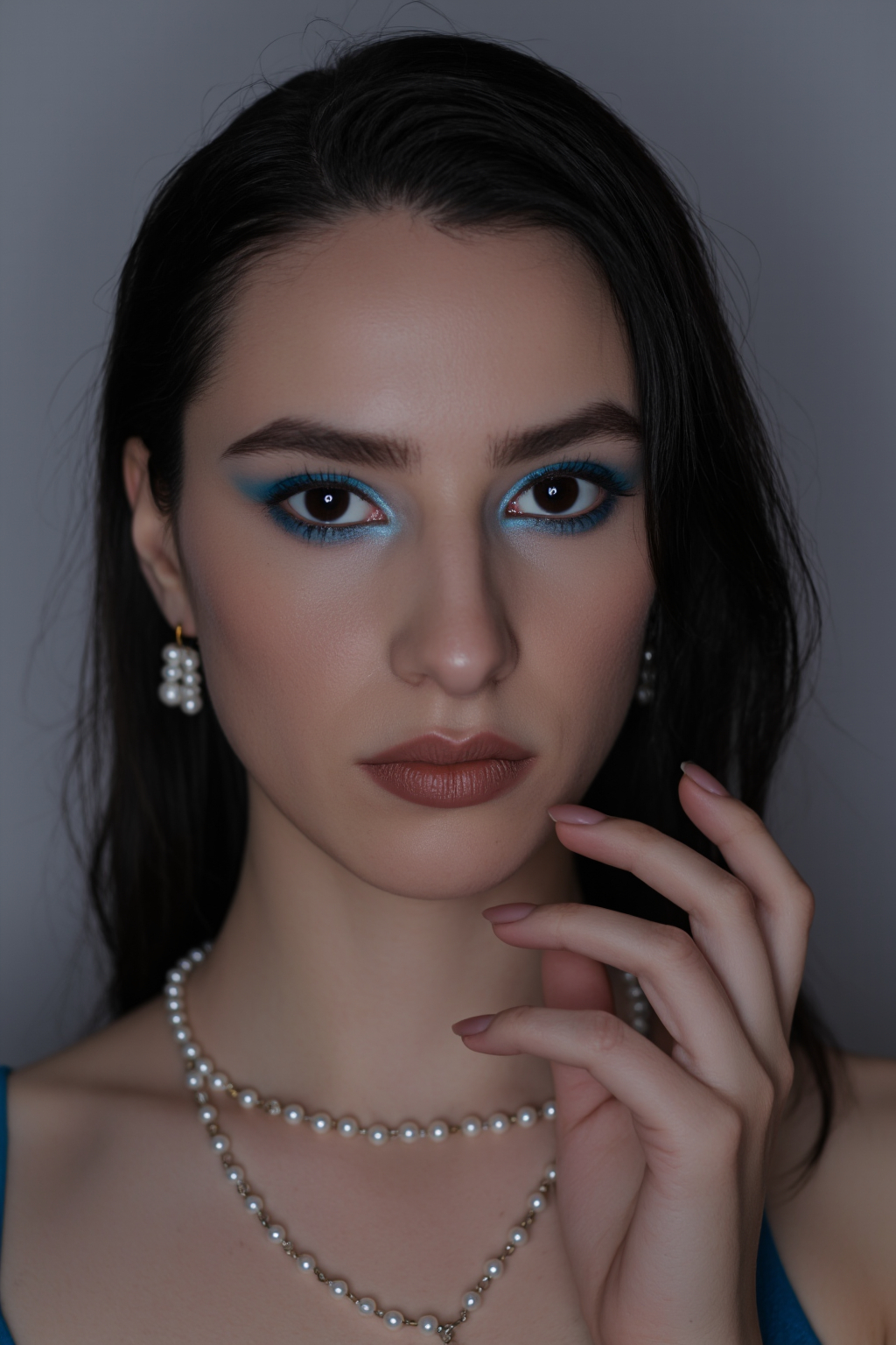 Pale Skinned Woman With Dark Hair Blue Blue Eyeshadow And Pearl Necklaces Set Against