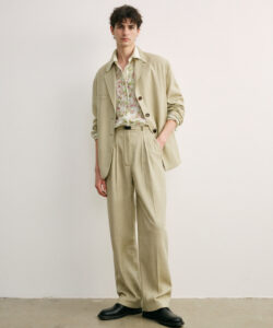 Slender Young Man In Beige Suit Floral Shirt Black Shoes Standing Against Plain White