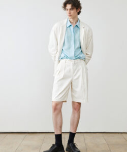Tall Slim Young White Man In A Light Blue Shirt White Jacket Beige Shorts Black Shoes