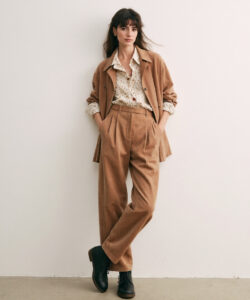Woman In A Beige Suit White Polka Dot Blouse And Black Boots Standing Against A Plain