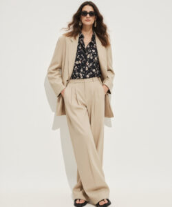 Woman In Beige Suit Black Floral Shirt Sunglasses And Black Sandals Standing Against A