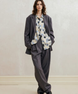 Woman With Wavy Hair Wearing A Gray Suit Floral Blouse Pearl Necklace Standing Against
