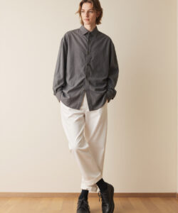 Young Man With Light Brown Hair Wearing A A Grey Shirt White Pants Black Shoes Against